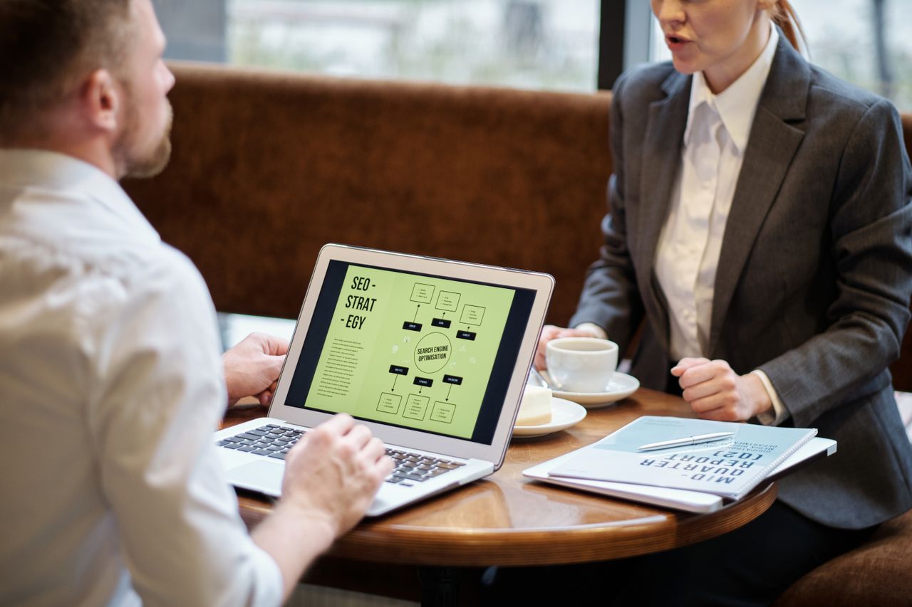 services-04 A man and woman engaged in a business meeting discussing SEO strategy in a cozy cafe setting.